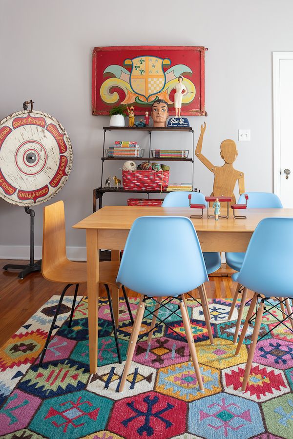 Colorful rug with modern craft table, antique pie shelf for storage, vintage game wheel and carousel panel as wall decor.