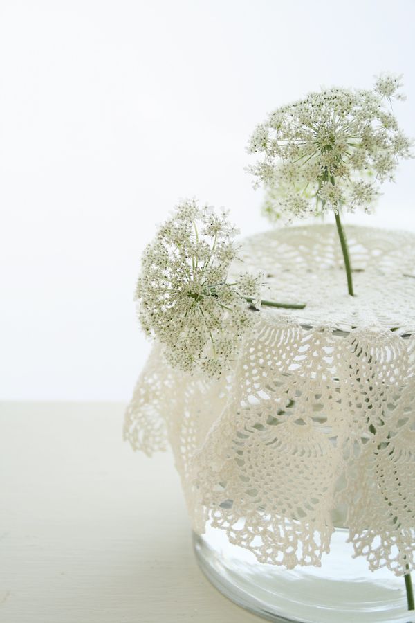 Small doily draped over a glass of water with a slender-stem flower.