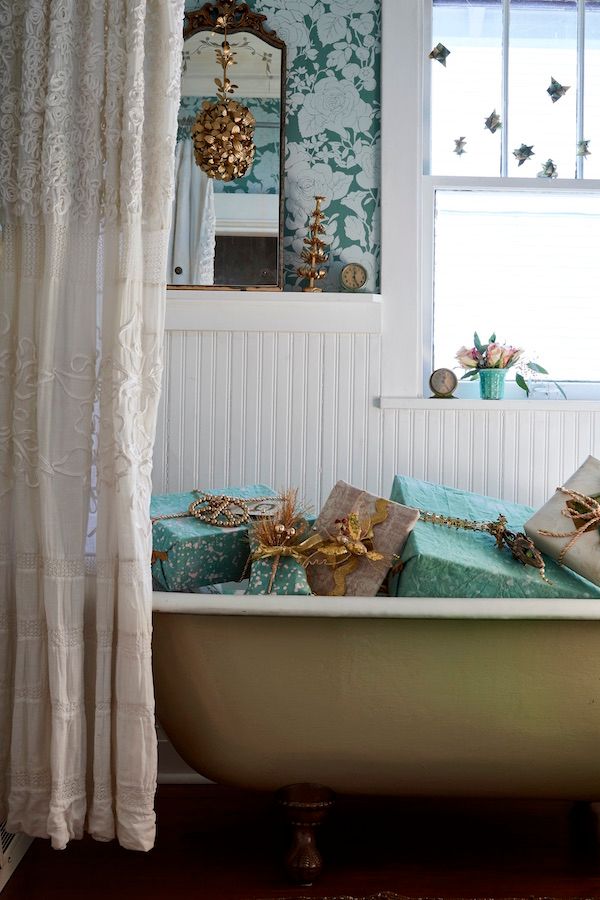 Clawfoot tub spray painted gold filled with turquoise and gold wrapped gifts. White beaded board wall and floral wallpaper.