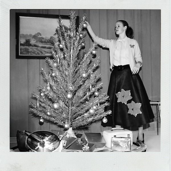 Vintage black and white image of lady in skirt decorating aluminum tree.