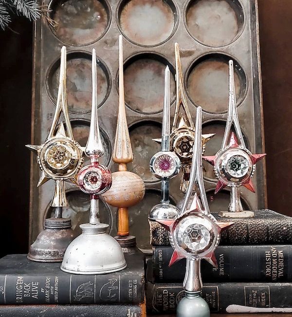 Old oil cans displaying vintage ornament Christmas tree toppers.
