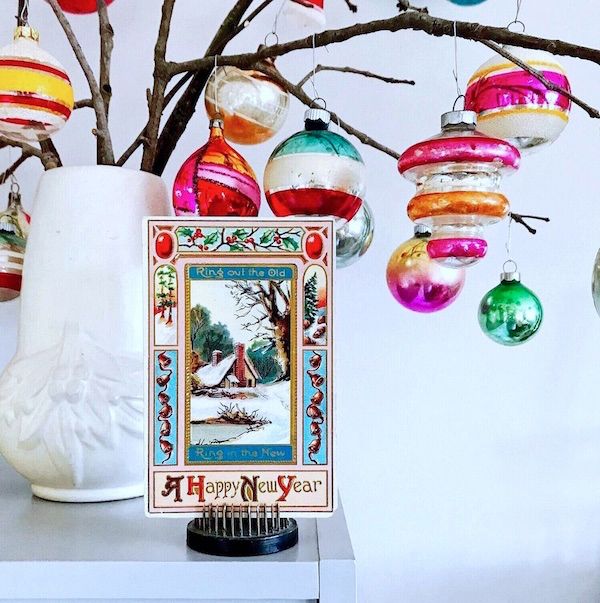 Branches in white vase holding vintage ornaments. Flower frog displaying a holiday postcard.