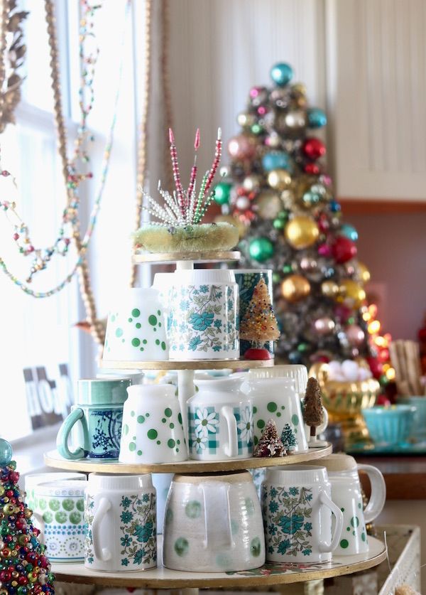 Vintage mugs on tiered stand with decorated tree in background.
