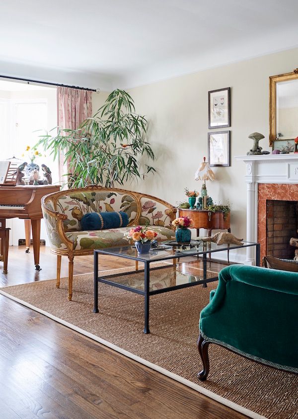 Antique curve-backed sofa with glass cocktail table in living room with vintage accessories.