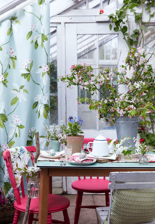 Spring table with crab apple blossoms, floral plates and painted pink chairs.