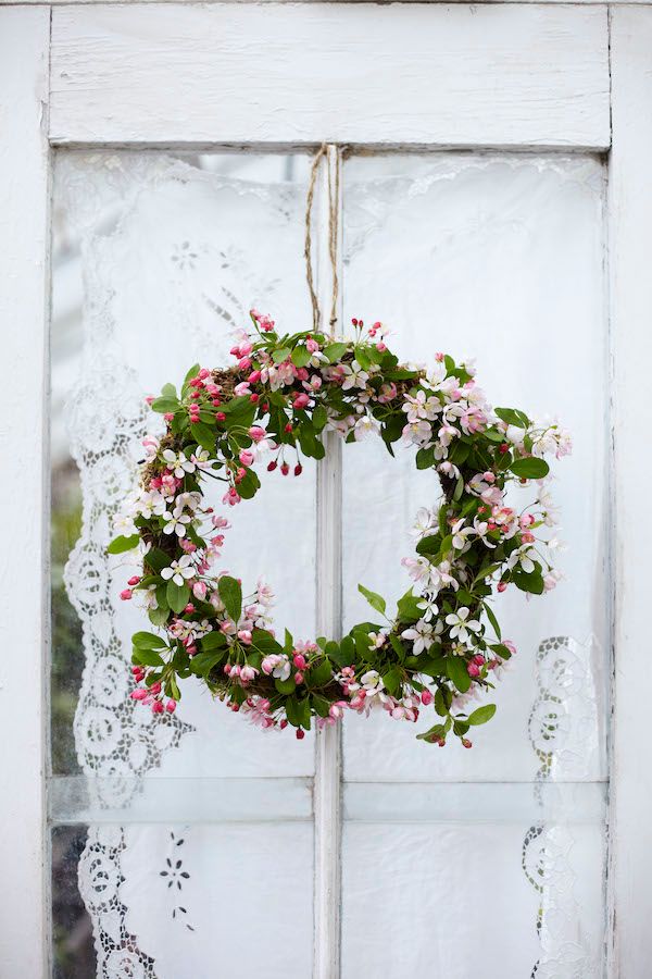 Crab apple blossom wreath hanging on window with lace covering.