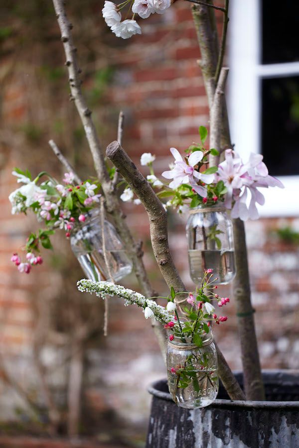 Crab apple blossoms and flowers in vintage jars hanging from sticks outdoors.