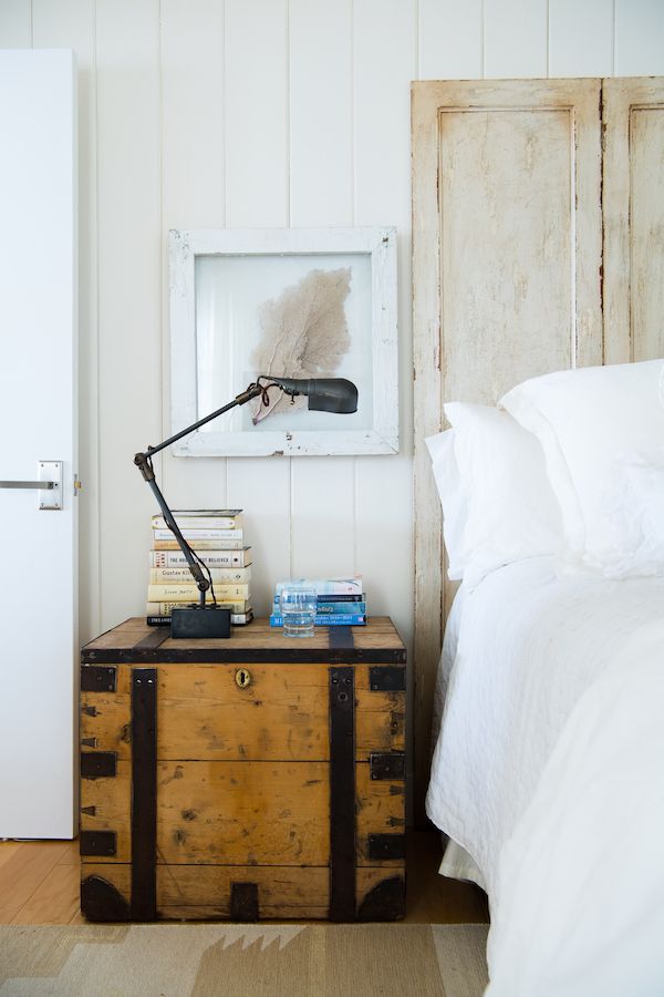 Unfinished old chest used as a nightstand in breezy white bedroom.