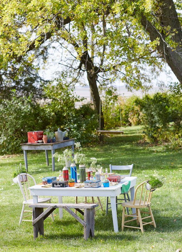 Potting party outdoors with vintage furniture and old tin lunch boxes for planting.