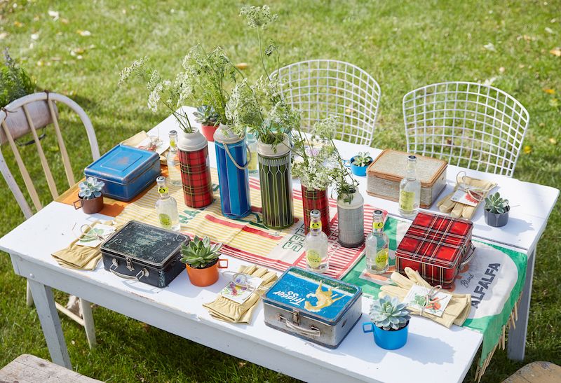 Outdoor potting party with vintage tin lunchboxes for planting and old thermoses with flowers as centerpieces.