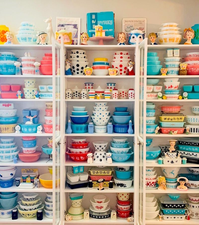 Large collection of Pyrex displayed in glass-doored shelving unit.