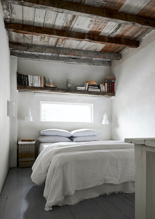Bedroom with white linens, vintage books and rustic wood beam ceiling.